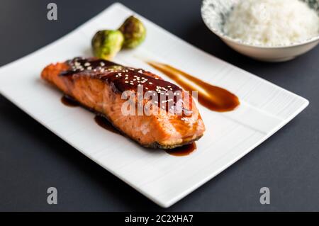 Cucina giapponese ispirato a piatti fatti di filetto di salmone alla griglia smaltato in deliziosa salsa teriyaki (base di salsa di soia) e germogli di Bruxelles su piatto bianco. Foto Stock