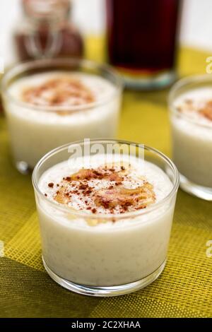Dessert al budino di riso al cocco con frizzle di sidro d'acero sulla parte superiore e cannella cosparsa servita in una ciotola di vetro. Orientamento verticale. Foto Stock