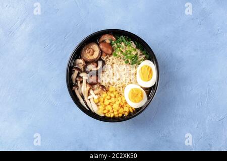 Zuppa di ramen noodle. Tagliatelle di Soba con uova, shiitake e funghi enoki, mais dolce e scalioni, colpo di testa su uno sfondo di ardesia Foto Stock