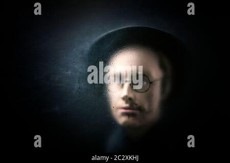 Personaggio misterioso con cappello e bicchieri dietro un vetro polveroso graffiato. Foto Stock