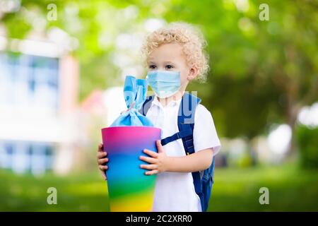 Il primo giorno scolastico, il bambino indossa una maschera facciale con cono caramella tedesco tradizionale. Torna a scuola in epidemia di virus. Studente con zaino e libri Foto Stock