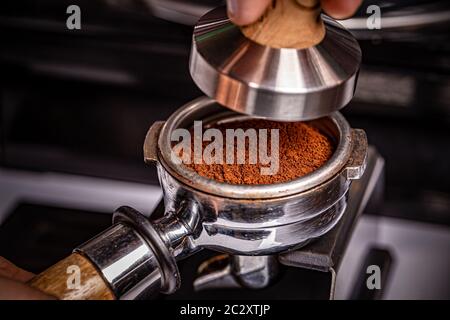 Barista è utilizzando un dispositivo antimanomissione per premere appena macinato di caffè del mattino Foto Stock