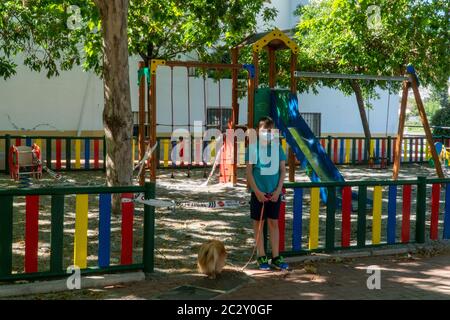 Un bambino triste sta in piedi nel parco giochi per bambini in quarantena. COVID-19 misure di sicurezza e protezione nel parco cittadino. Foto Stock
