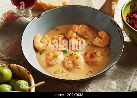 Close-up su scampi aragoste di formaggi-salsa panna nel vecchio piccolo tegame con olive e bicchiere di vino in uno stile rustico ristorante Foto Stock