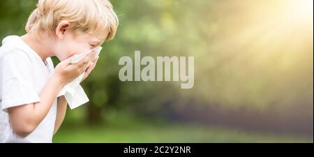 Bambino con allergia in natura mentre starnutisce in un fazzoletto Foto Stock