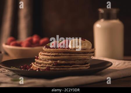 Pancake con lamponi, fette di banana, semi di melograno e miele su tavola d'annata in legno. Foto Stock