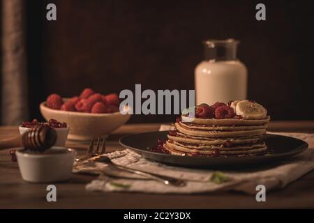 Pancake con lamponi, fette di banana, semi di melograno e miele su tavola d'annata in legno. Foto Stock