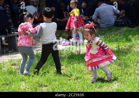 Pyongyang, Corea del Nord - 1 maggio 2019: Felici i bambini che si divertono all'aperto sul prato verde mentre i loro genitori riposano all'ombra. Mettere a fuoco su un acceso Foto Stock