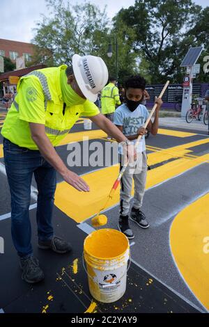 Il direttore della città di Austin, Robert Spillar, insegna a Tobias Jackson-Woods come utilizzare un rullo di vernice mentre gli artisti dipingono un murale sulla East 11th Street vicino al centro di Austin, che dice "Black Artists Matter", due giorni dopo che il gruppo ha dipinto "Black Austin Matters" in grandi lettere gialle su Congress Avenue in il cuore del centro. Foto Stock