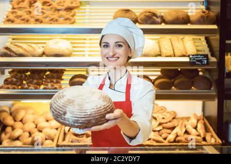 Commessa con grembiule presentando il pane fresco in un panificio che guardando nella telecamera Foto Stock