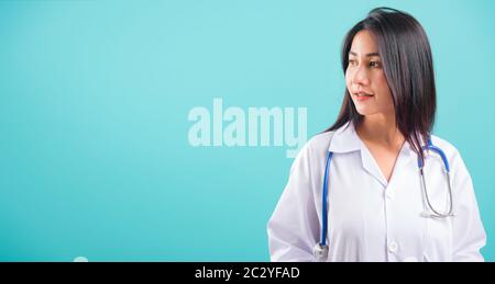 Ritratto asiatico bella donna medico sorridente suo stare con Le Mani in tasche su sfondo blu, con spazio copia per il testo Foto Stock