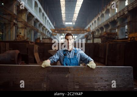 Lavoratore maschile in uniforme e guanti in stack di pezzi metallici in fabbrica. Industria metallurgica, produzione industriale di prodotti siderurgici Foto Stock