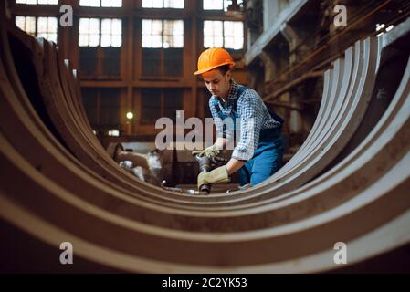 Lavoratore maschile in uniforme e casco rimuove la bilancia da pezzi di metallo in fabbrica. Industria metallurgica, produzione industriale di prodotti siderurgici Foto Stock