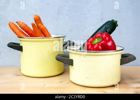 peperone, zucchine e carote in pentole rustiche su tavolo di legno con fondo grigio Foto Stock