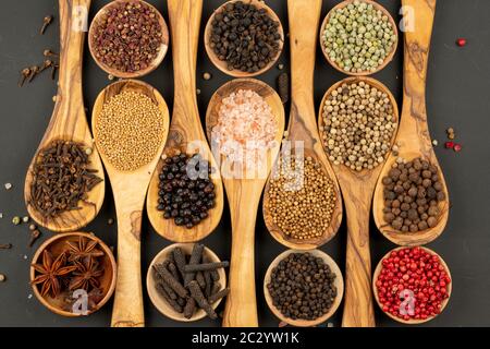Spezie e cibo - sfondo fatto di molte varietà di spezie e pepe in piccole ciotole di legno e cucchiai di cottura in legno di oliva su una ba nera Foto Stock
