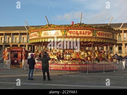 La gente si fermò a guardare una giostra d'epoca nelle vacanze di natale nella piazza pubblica di Halifax Piece Hall West yorkshire Foto Stock