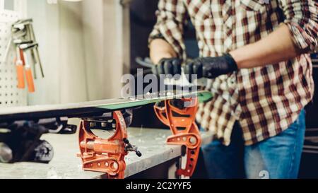 Manutenzione sci. Rimozione della cera in eccesso dal raschietto in plastica della base da sci. Servizio sci e riparazione. Lavoratore negozio invernale che fa base r Foto Stock