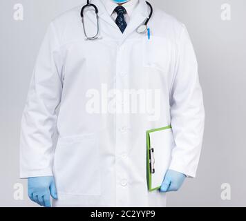 medico maschile in un cappotto bianco, guanti in lattice blu, uno stetoscopio appeso al collo, medico che tiene un porta-carta verde con un foglio bianco vuoto Foto Stock