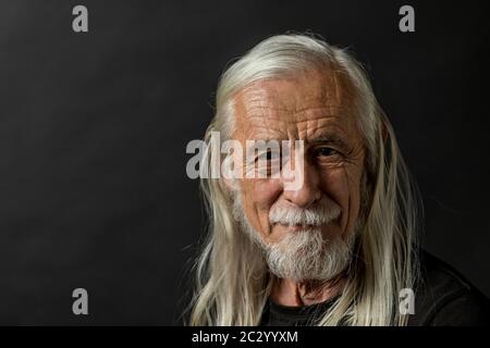 Tasto basso ritratto di interessante a lungo i capelli grigi vecchio uomo guardando la fotocamera con tranquillità. Foto Stock