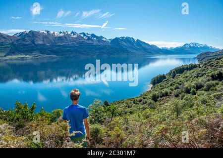 Giovane uomo che guarda sul lago Wakatipu, montagne riflesse nel lago, Otago, Isola del Sud, Nuova Zelanda Foto Stock