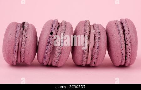 quattro macaroni dessert con farina di mandorle viola rotonda e crema su sfondo rosa, torta deliziosa, primo piano Foto Stock