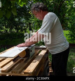 Uomo caucasico senior utilizzando sega circolare per tagliare la tavola di parquet in giardino Foto Stock