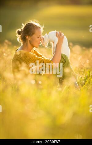 Piuttosto, giovane donna con il suo gatto Pet sitting in erba sul bellissimo prato illuminato dalla calda luce della sera (SHALLOW DOF; dai toni di colore immagine) Foto Stock