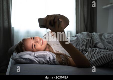 Bella, giovane donna che dorme nel suo letto con il suo cellulare vicino a lei. Smartphone in Bed Mobile / smartphone Addiction Concetto. Foto Stock