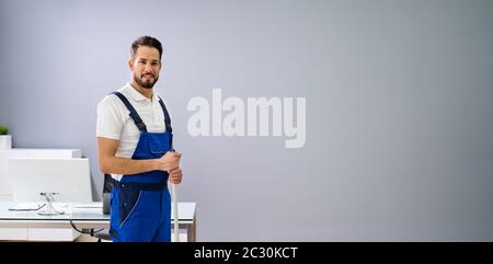 Ritratto Di Giovane Uomo Felice In Piedi Con Attrezzatura Di Pulizia In Ufficio Foto Stock