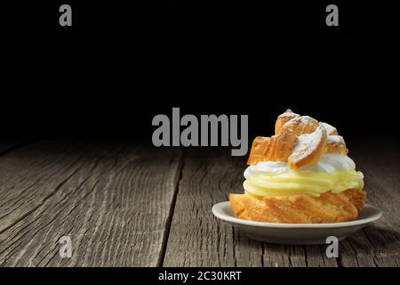 Un profiterolo, decorato con uno spolverato di zucchero in polvere e riempito con abbondante crema di crema, è adagiato su un piccolo piatto di ceramica. Foto Stock