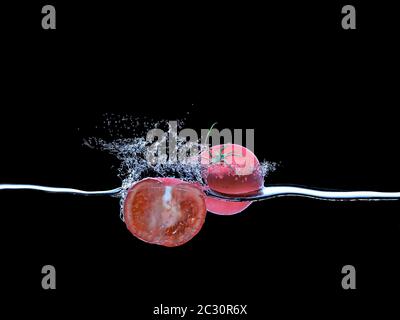 pomodori che cadono in acqua e spruzzi su nero. concetto di cibo fresco e sano. rendering 3d. Foto Stock