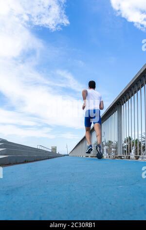 Giovane corridore con pantaloni blu e t-shirt bianca che corre al sole su una pista blu. Concetto di motivazione, carriera Foto Stock