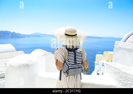 Giovane donna in un abito bianco e cappello di paglia, a piedi nella città di Oia, isola di Santorini, Grecia Foto Stock