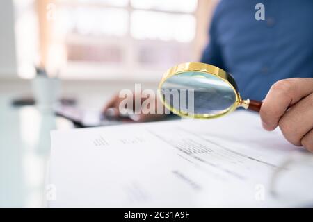 Primo Piano Delle Fatture Per L'Esame Delle Mani Da Parte Degli Uomini D'Affari Con Lente D'Ingrandimento Alla Scrivania Foto Stock