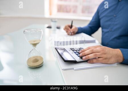 Close-up di clessidra di fronte ai mediatori la mano della fattura di calcolo Foto Stock