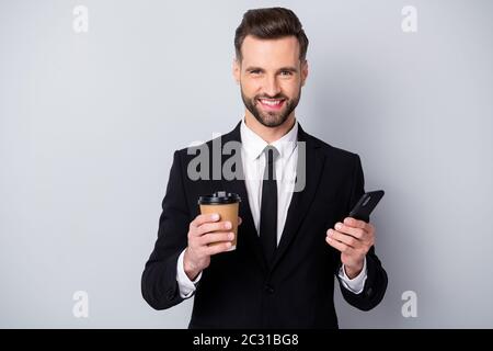 Ritratto di positivo affascinante uomo commerciale tenere take-away americano tazza bevande calde utilizzare il suo smartphone sempre connesione concetto indossare giacca nera Foto Stock