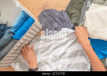 Stoccaggio verticale di indumenti, metodo di riassetto Marie Kondo, concetto di pulizia della stanza. Mani donna che si riordinano e si ordinano i vestiti nel cesto. Vista dall'alto Foto Stock