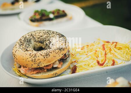 Piatto proposto in una festa gastronomica composta da un bagel con semi e farcito con frutti di mare con patatine di paglia Foto Stock