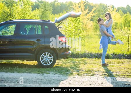 Bell'uomo che carrava la sua ragazza sorridente sul retro vicino all'auto al tramonto Foto Stock