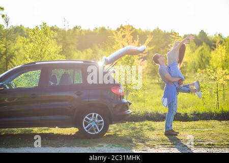 Bell'uomo che carrava la sua ragazza sorridente sul retro vicino all'auto al tramonto Foto Stock