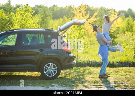 Bell'uomo che carrava la sua ragazza sorridente sul retro vicino all'auto al tramonto Foto Stock