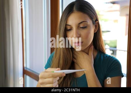 COVID-19 Pandemic Coronavirus mal di gola tosse secca febbre preoccupazione Donna controllo della temperatura con termometro a casa sintomo di SARS-cov-2. Controllo ragazza Foto Stock