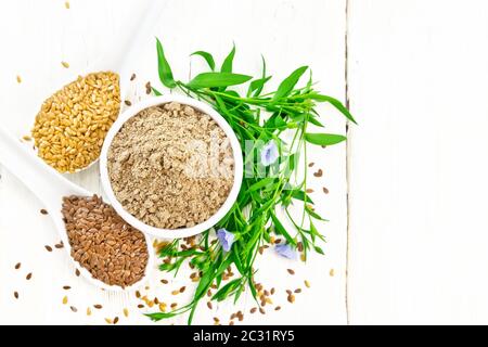 Farina di lino in una ciotola, bianco e marrone e i semi di lino in due cucchiai e su tavola, foglie e lino blu fiori su tavola di legno del fondo da sopra Foto Stock