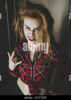 Ragazza con frugoso sorriso divertente hairdo e mostra gesto per rock Foto Stock