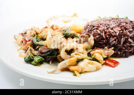 Piccante, soffritto di calamari fritti con foglie di basilico e peperoncino, uova sunnite con il lato alto, servite con riso marrone. È Foto Stock