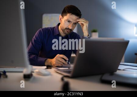 Sottolineato ragioniere seduto con la testa tra le mani mentre si lavora fino a tardi in ufficio Foto Stock