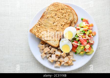 Cibo pulito in stile moderno, burro di arachidi con pane, uova sode, pollo alla griglia e avocado, fragola Foto Stock