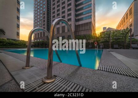 L'area piscina dell'hotel e gli edifici della città di Bangkok al tramonto Foto Stock