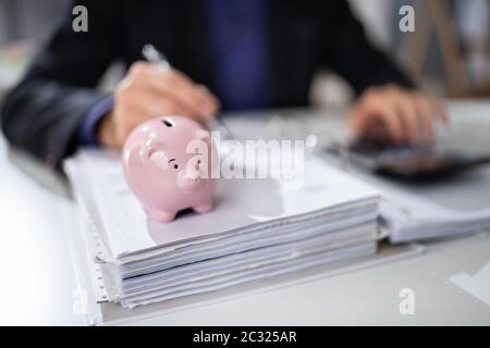 I mediatori controllo fattura con Rosa Piggybank sulla scrivania Foto Stock