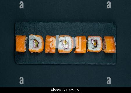 Tavola Granit con sushi, ripiena di panini di vario tipo, accanto a bastoncini per sushi, marinaginger rosso e salsa di soia. Viste dall'alto Foto Stock
